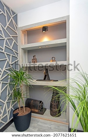 Beautiful corner in interior decorated with grey wall with abstract pattern, green plants in pots and ancient home stuff on wooden shelves Royalty-Free Stock Photo #2077621651