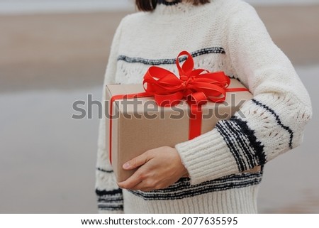 a happy European woman in a Santa Claus hat holds a gift in a box with a red ribbon and her labrador dog in a deer costume against a snowy landscape. New Year's gifts or for a birthday. celebrating