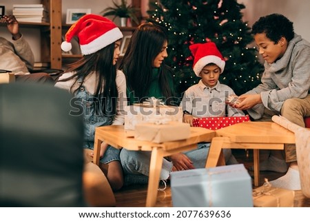 Happy multiethnic family sitting at home on the floor in front of the Christmas tree and opening gifts on Christmas eve.