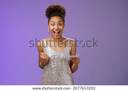 Excited charming young african-american woman lucky winning game playing smartphone standing pleased yelling happily clench fist triumphing joyfully celebrating great news received message Royalty-Free Stock Photo #2077653202