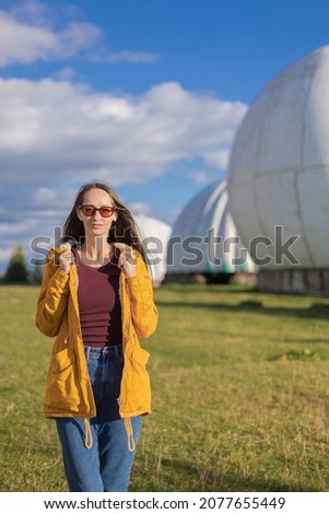 A girl with long hair in yellow clothes poses at sunset against the background of the white spheres of an old Soviet radar station in the Carpathians. Summer, sunny.