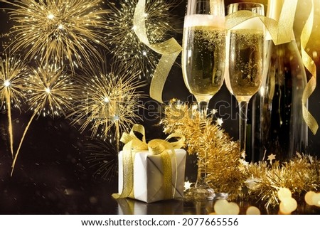 New year's eve party celebration background with sparkling wine glasses and bottle decorated with gift ribbons and golden decoration on black table and fireworks background. Top view