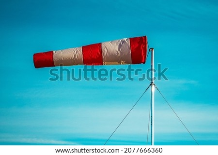 Red-white windsock against the blue sky in sunny weather. Wind vane indicates the strength and direction of the wind
