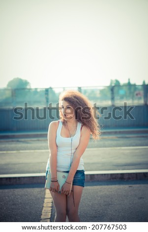 young beautiful long curly hair hipster woman listening to music with tablet in the city