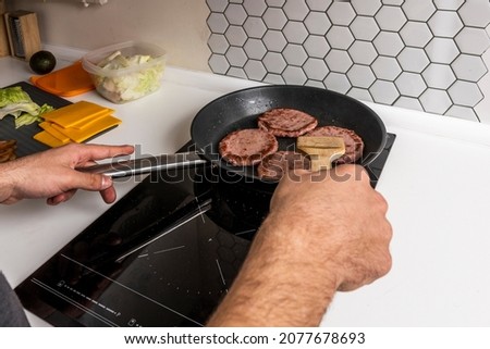 Young man's hands cooking beef burgers in a non-stick frying pan
