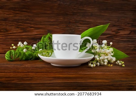 Cup of green tea with lily of the valley or may bells flowers and fern leaves on a wooden background. Copy space. Top view.