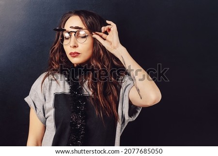 Close up studio portrait of seductive curly hipster girl with closed eyes touching glasses with hand, on a black background