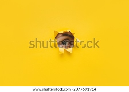 One eye looking through a hole in a yellow paper. Voyeurism. Woman is watching the husband. A curious look. Jealousy, spying on or overhearing the concept. Copy space. Royalty-Free Stock Photo #2077691914