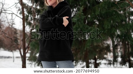 Horizontal banner with a model in oversized black hoodie in winter park.front view.fashion and wear concept.warm oversize wear at woman.space for text and logo.mock up for print.female standing 