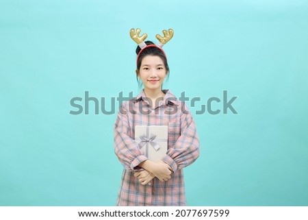 Portrait Cheerful cute girl holding giftbox smiling wearing reindeer headband isolated blue color background. Christmas and new year sales joy concept