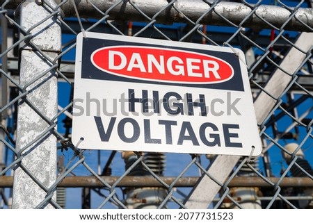 Danger High Voltage sign on chain link fence with power generators in the background.