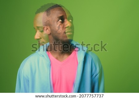 Studio shot of young African man wearing blue jacket with pink shirt against green background