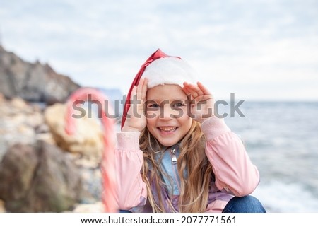 Little pretty girl in a santa claus hat on the seashore, a child walks in a jacket