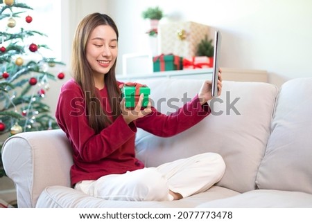 Asian women celebrate Christmas festival. Female teen holding Gift and using smartphone selfie in living room at home.