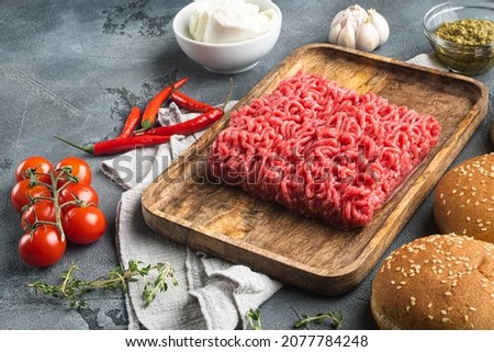 Fresh raw minced beef steak burgers with spices ingredients set, on wooden tray, on gray stone background