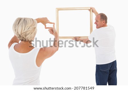 Mature couple hanging up picture frame on white background