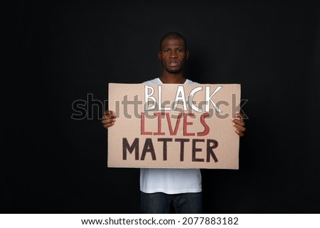 African American man holding sign with phrase Black Lives Matter on dark background. Racism concept