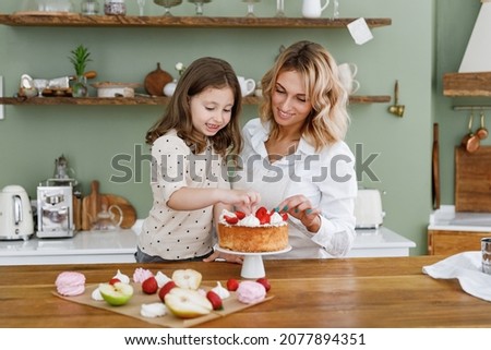 Happy chef cook baker mom woman in white shirt work with child baby girl helper decorate adorn pie with berries at kitchen table home Cooking food concept Mommy little kid daughter prepare fruit cake. Royalty-Free Stock Photo #2077894351