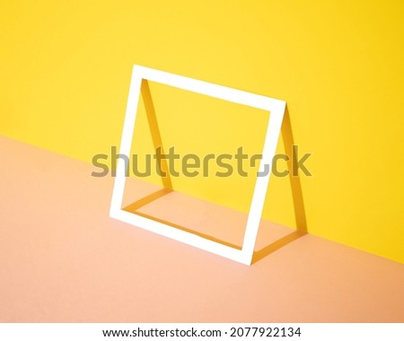 White square frame leaning against a yellow and pink background. Minimal design and concept. Copy space.