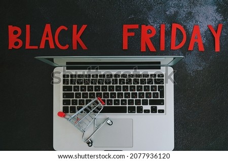 Black Friday concept. Inscription "black friday", laptop, coffee cup, mini shopping cart on black background. Copy space, top view, flat lay. Creative holiday flyer. Online sale and discounts