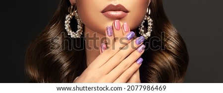 Beautiful woman showing multicolored designer manicure nails  and stylish jewelry  earrings .Makeup and cosmetics. Brunette  girl with long  and   shiny curly hair Royalty-Free Stock Photo #2077986469