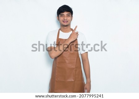 Happy young asian man barista waitress pointing with fingers to different directions isolated on white background
