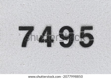 Black Number 7495 on the white wall. Spray paint. Number seven thousand four hundred ninety five.