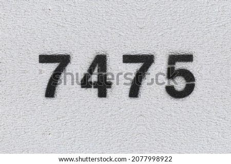 Black Number 7475 on the white wall. Spray paint. Number seven thousand four hundred and seventy five.