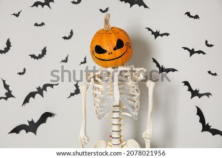 Skeleton with pumpkin head and paper bats on white wall