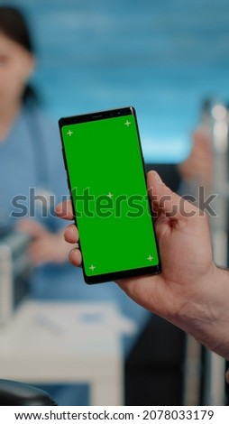 Close up of nurse vertically showing phone with green screen to senior patient living in nursing home. Medical specialist holding smartphone with chroma key and isolated mockup template
