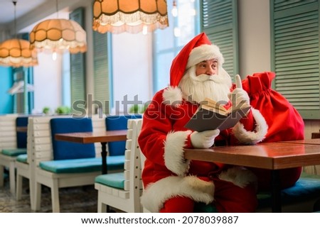 Santa Claus is sitting in a cafe and reading a book