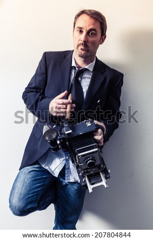 Photo of a photographer in his forties with an old 4x6 camera and holding a cigar.  Filtered for more retro feel. Motion blur on hands.