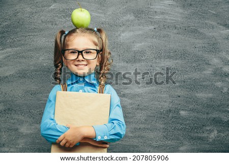 Cheerful smiling little kid (girl) against chalkboard. Looking at camera. School concept