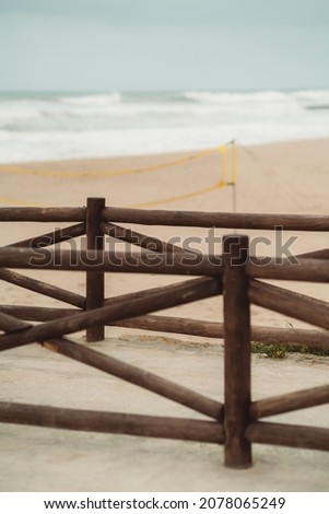 A vertical shot with a shallow depth of field of a brown wooden fence made of round timbers on the evening beach with the ocean waves and water in a defocused background