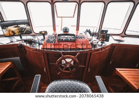 A cockpit area inside of a deckhouse of a retro safari or cruise yacht with a control panel on the wooden base and many navigation devices: compass, radio transceiver, radars, surveillance, dashboards Royalty-Free Stock Photo #2078065438
