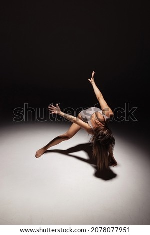 Expression, energy. Dynamic portrait of young flexible contemp dancer dancing isolated on dark studio background in spotlight. Art, motion, action, flexibility, inspiration concept. Solo performance
