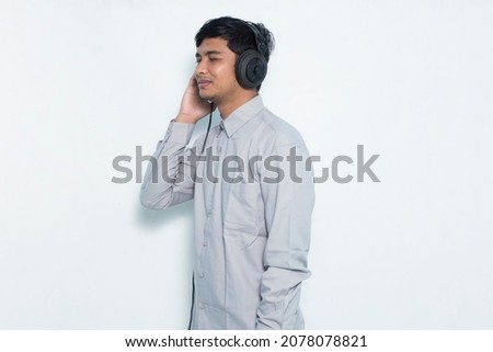 Young asian man listening music with formal outfit on white background
