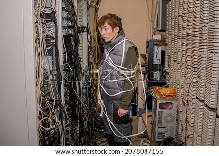 There is a technician wrapped in wires in the server room. A lot of wires are in the racks of the old data center Royalty-Free Stock Photo #2078087155