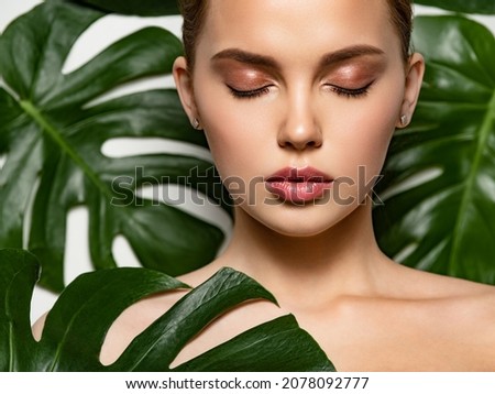 Closeup face of young beautiful woman with a healthy clean skin. Beautiful white girl with big green leaves. Beauty and spa treatment concept. Pretty woman with natural makeup and plant near face Royalty-Free Stock Photo #2078092777