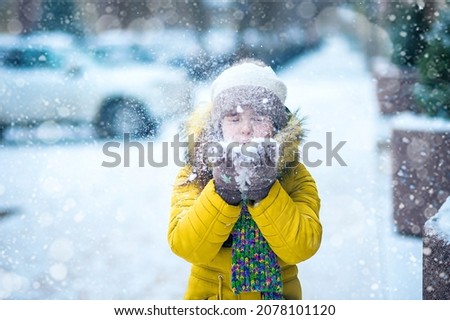 Happy girl in yellow jacket plays with snow. Children games in winter.