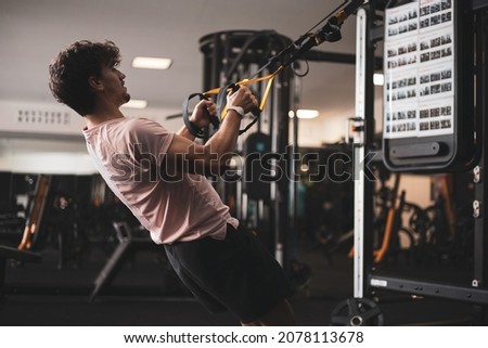 a young man doing sports with a trx in a gym.