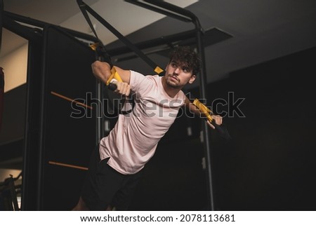 a young man doing sports with a trx in a gym.