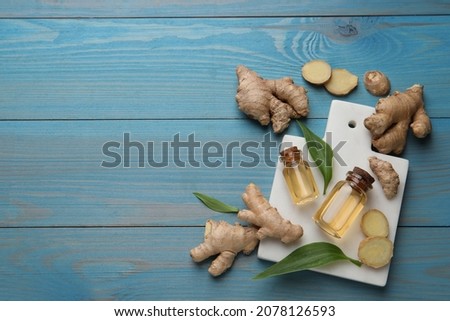 Glass bottles of essential oil and ginger root on light blue wooden table, flat lay. Space for text
