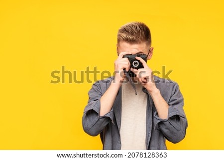 Young guy in medical mask taking photo on retro camera isolated on yellow background. Space for text