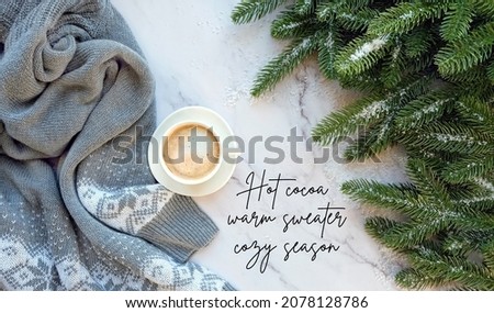 Christmas background. quote "Hot cocoa, warm sweater, cozy season". coffee cup, sweater, fir tree branches on marble table. Christmas, new year holidays concept. festive winter season. top view
