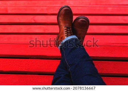 Men's feet in brown leather boots on a red background with space for text with space for text and your advertising