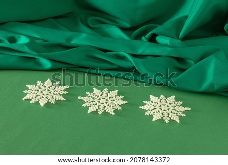 Creative Christmas composition with three white snowflakes on pastel green table against shiny curtain. Retro futurism scene.
