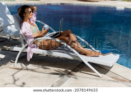 beautiful woman works on the computer near the pool. high quality photo