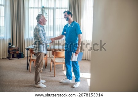 Pleased patient greeting his doctor in his house