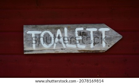 A closeup shot of a wooden arrow-shaped WC sign in Swedish on a red background